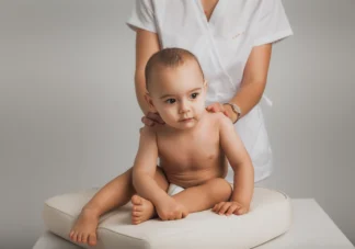 Chiropractor gently resting her hands on a seated baby's shoulders during a check